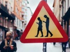 A humorous road traffic warning sign showing people looking down at their phones and not looking where they are going